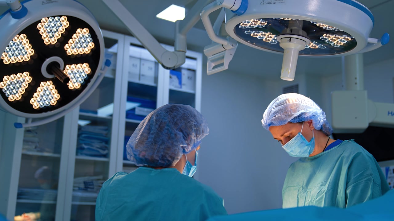 Two female medics stand under the round lamps in surgery room. Operation in modern hospital.