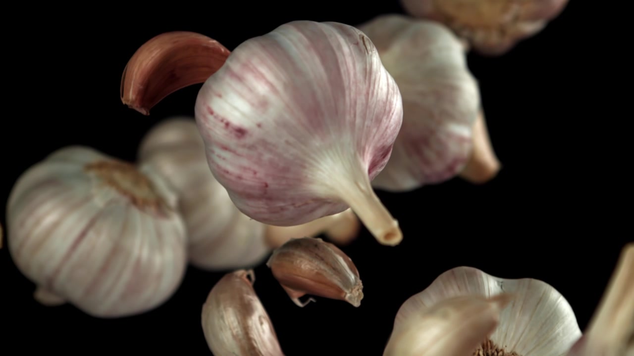 Bulbi e spicchi d'aglio freschi che cadono in super slow motion su sfondo nero