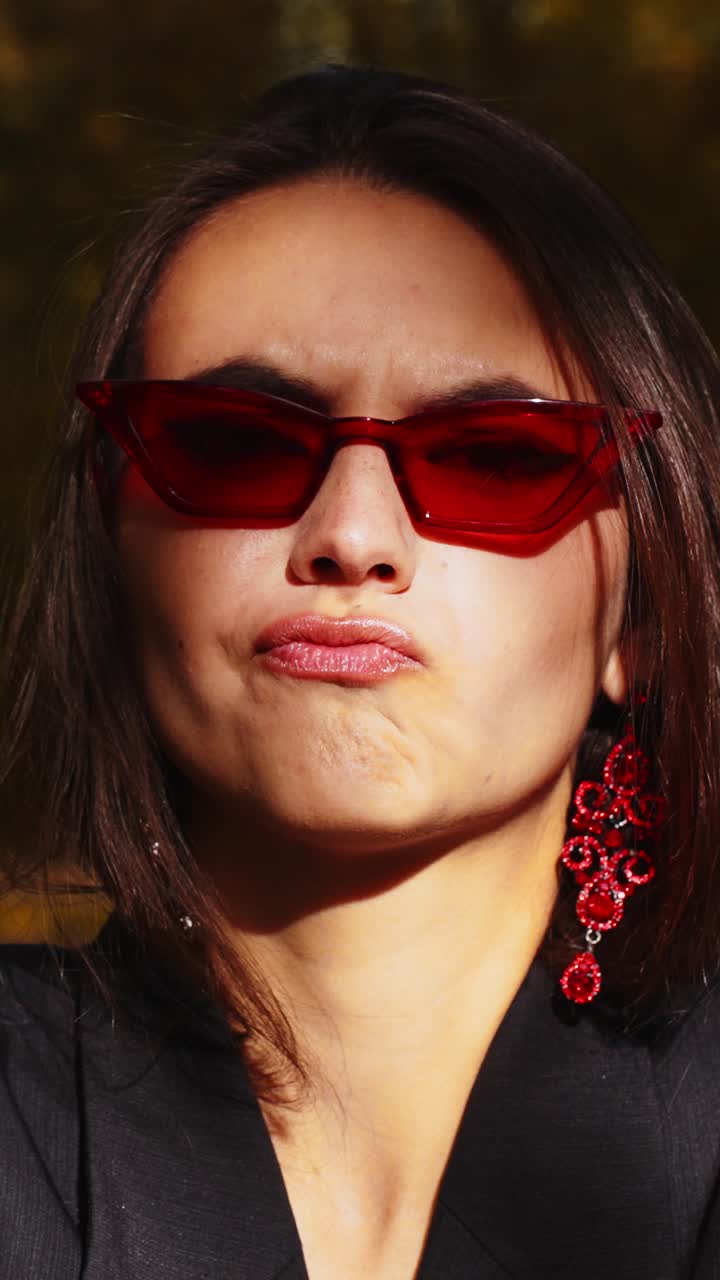A Confident Young Woman Showcases Her Style with Bold Red Sunglasses and Elegant Earrings, Effortlessly Blending Fashion and Attitude for a Striking Look