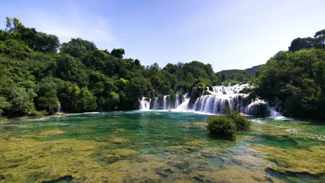 tilt up from colorful water to wide waterfalls and forest at krka