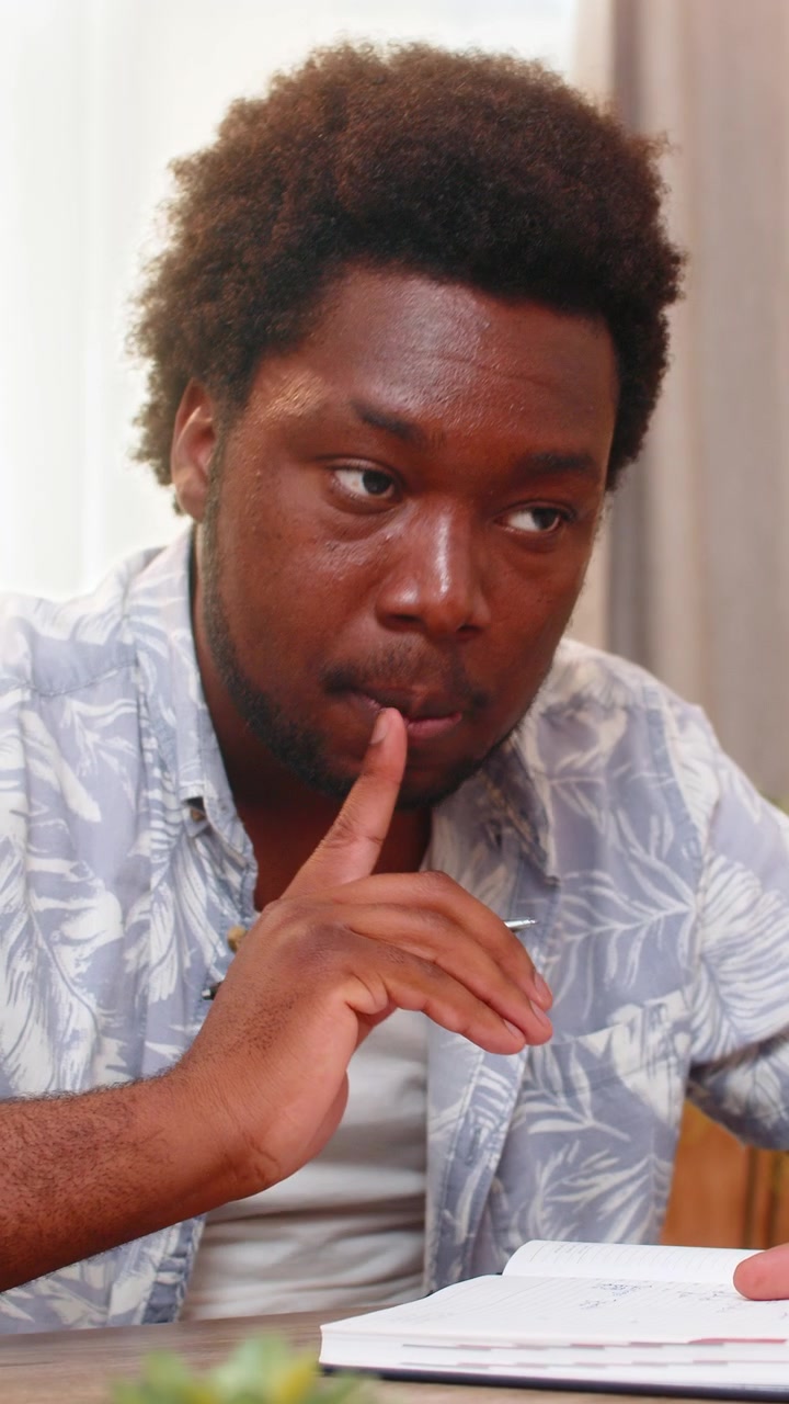 African american young man on home table writes plans in notebook and thinks carefully about goals