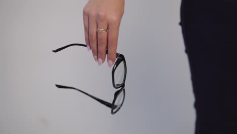 female hand is holding model of eyeglasses with black rim on a gray background