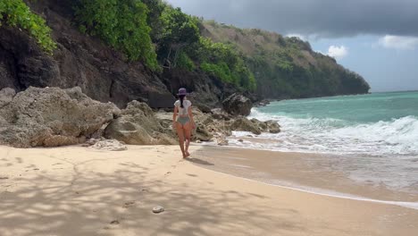 Tranquil-Paradise:-Young-Girl-in-Bikini-Walks-Barefoot-on-Secluded-Green-Bowl-Beach,-Bali