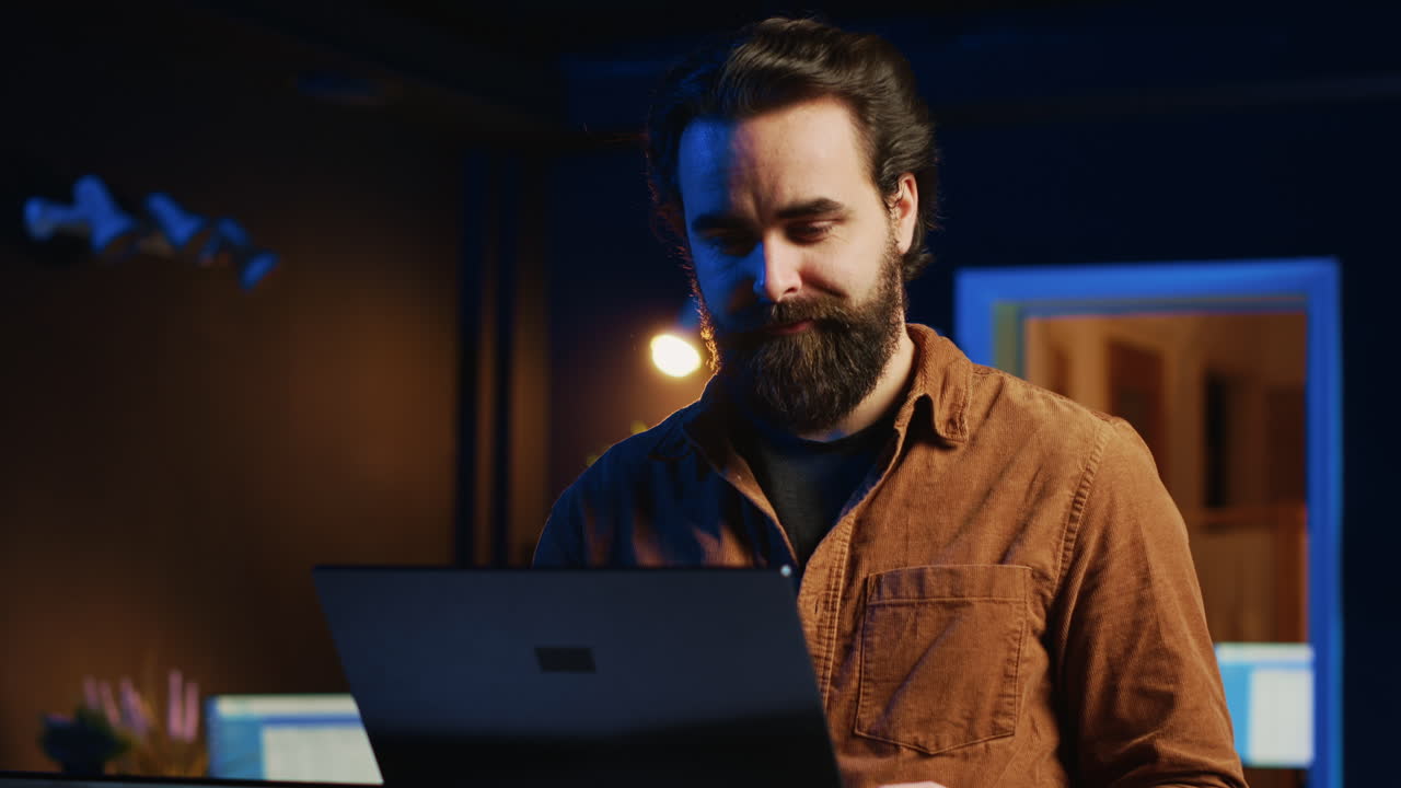 Remote IT support worker standing in home office, programming on laptop