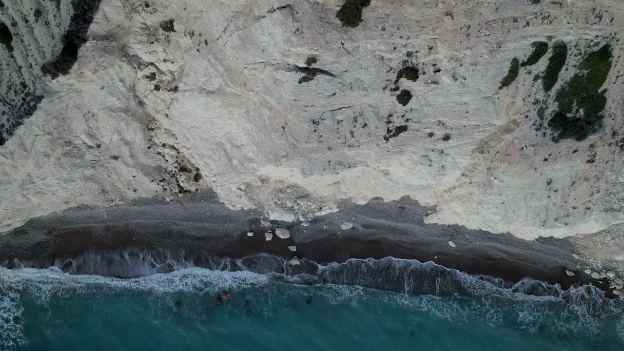las claras olas esmeralda rodan sobre los escarpados acantilados rocosos de la playa de kourion al atardecer en chipre - ascenso aéreo de arriba hacia abajo