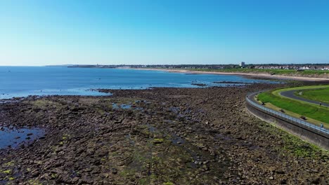 Panning-shot-of-rock-pools-and-coastline-during-summer-at-Whitley-Bay,-UK