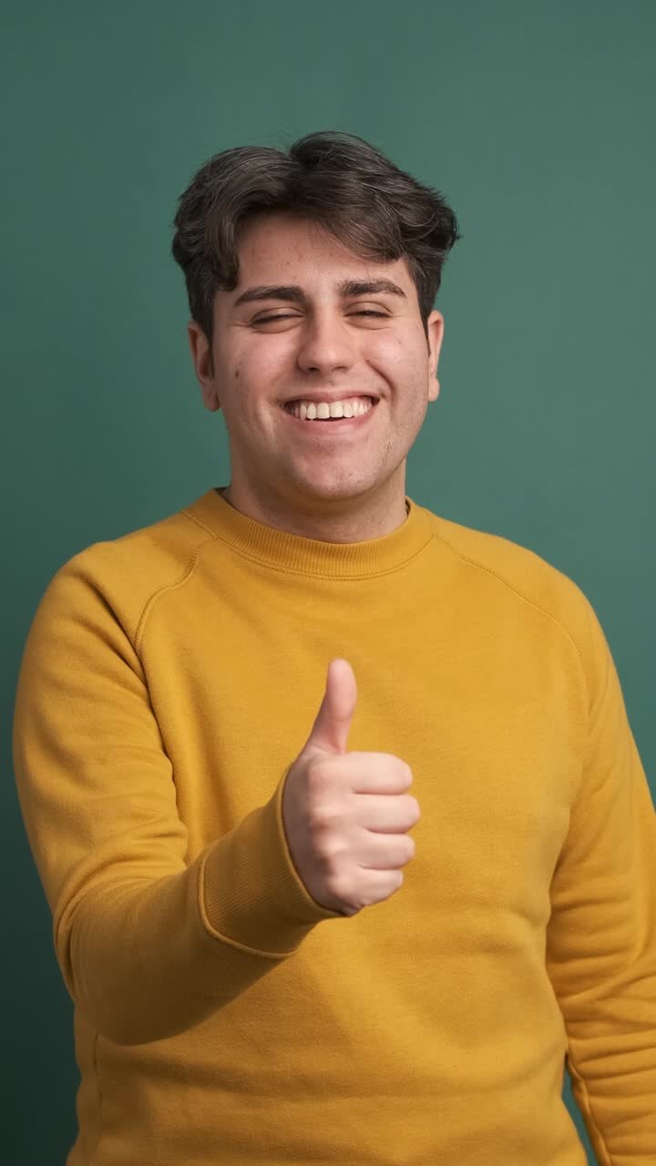 Uomo sorridente che mostra il pollice in alto nello studio verde