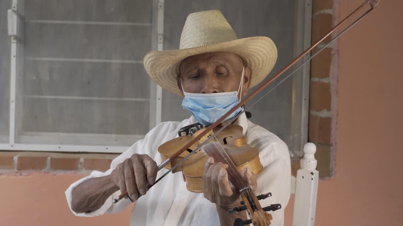 captura de pantalla de un músico de edad hispana con un sombrero y una máscara tocando el violín en la calle