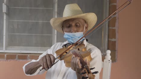 gros plan d'un musicien d'âge hispanique avec un chapeau et un masque jouant du violon dans la rue