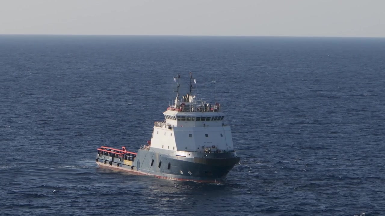 Aerial drone footage of an offshore support and supply tugboat navigating deep blue ocean waters