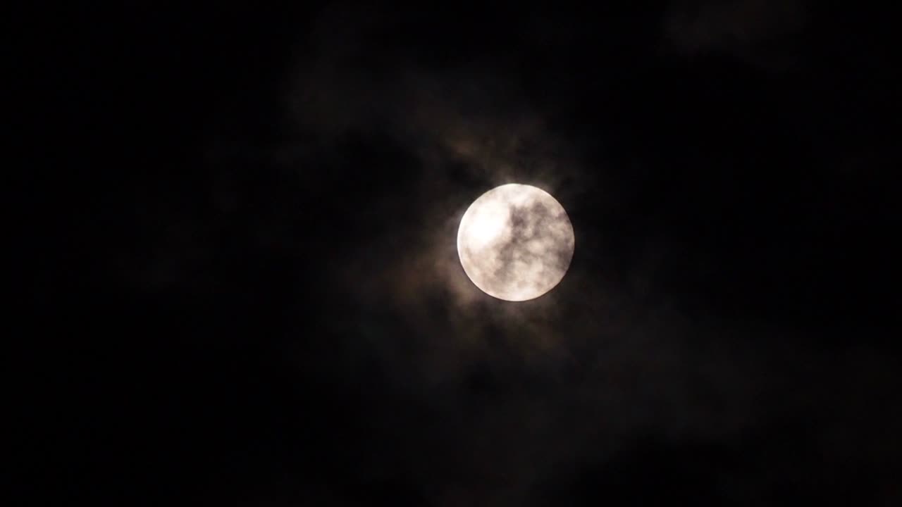 primer plano de la luna llena en una noche oscura con nubes moviéndose sobre ella. movimiento 4k b-roll imágenes