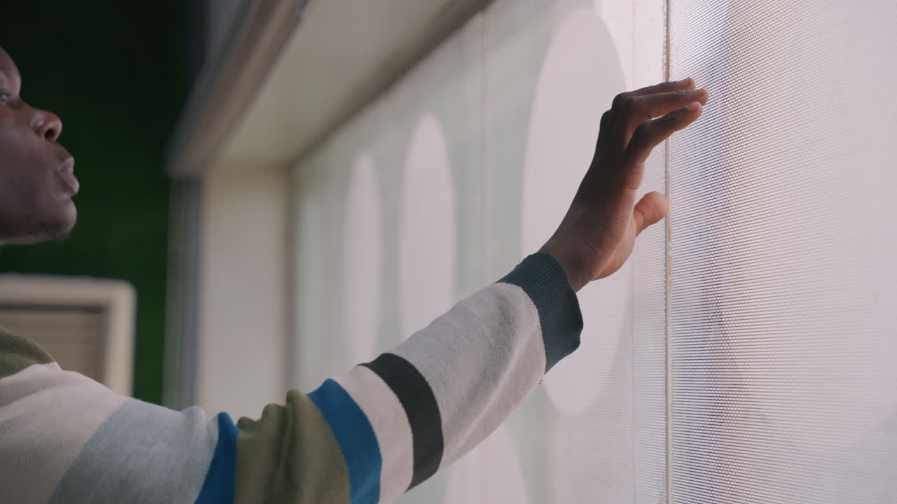 Hands exploring textured blind surface. Closeup of fingers tracing concentric pattern on sheer window blind, striped sleeve visible, studio apartment backdrop, tactile curiosity and design inspection