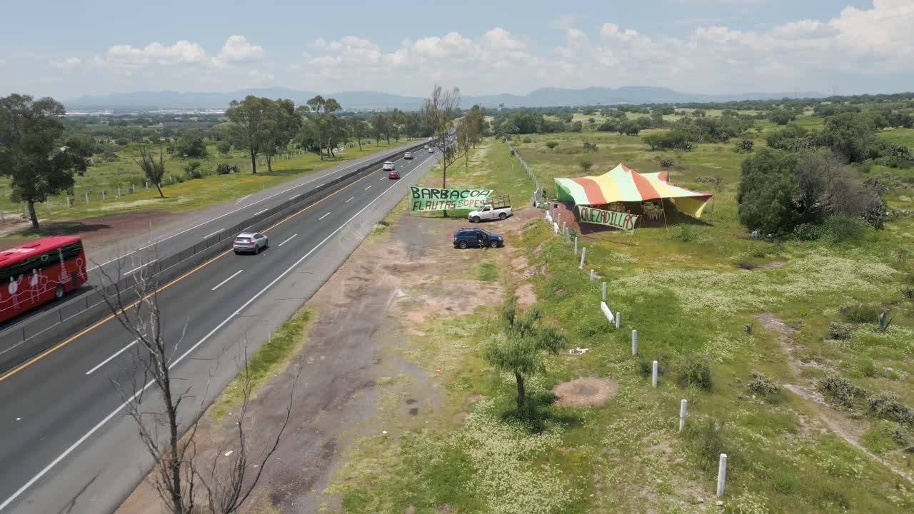 Slow Drone Aerial Pullback Revealing Roadside Barbacoa Stand in Green Farmland in Mexico – Backward Flight, Midday Sunny 4K