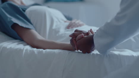 female patient lying in hospital ward and holding hands with doctor