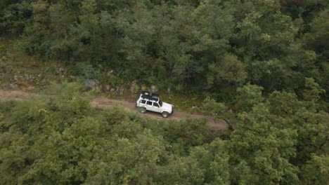 white cherokee truck on an adventure driving trough the woods in the mountains, aerial drone shot