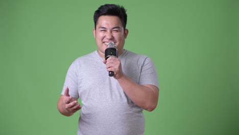 young handsome overweight asian man against green background