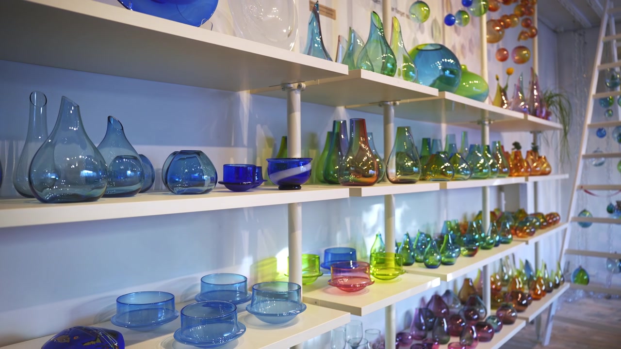 Inquadratura interna grandangolare di scaffali pieni di sculture e decorazioni colorate fatte a mano in cristallo di vetro, esposte in un negozio di artigianato locale nelle isole Lofoten.
