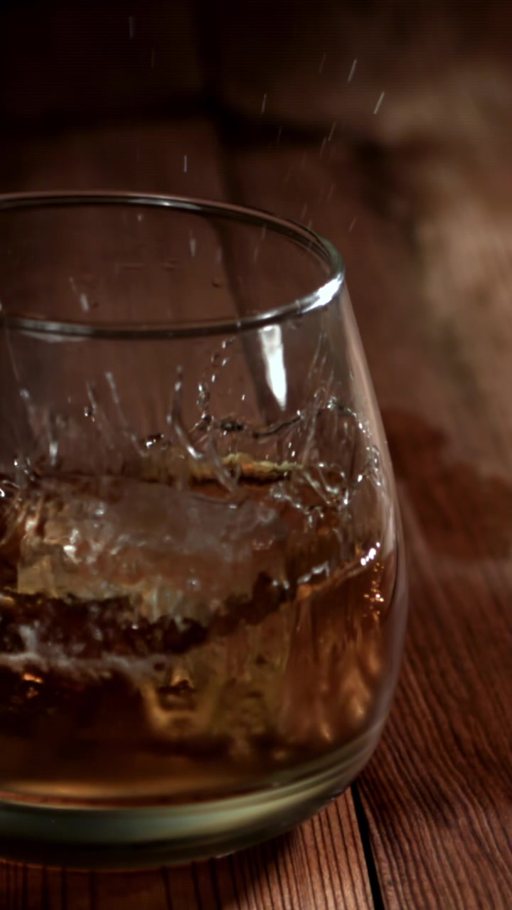 Caduta al rallentatore di un cubetto di ghiaccio in un bicchiere di whisky