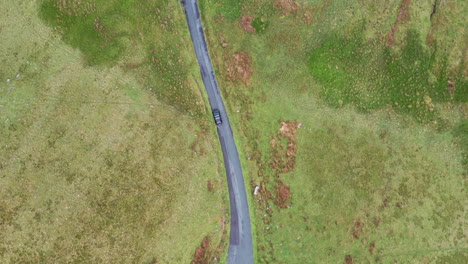 aerial top down view, following a black car driving on a rural road, bright day