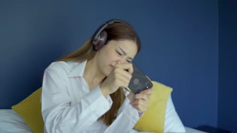 happy teen woman wearing headsets playing online game with a smart phone on a bed, female lost the game on smartphone.