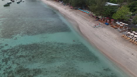 Person-swimming-off-beach-on-Gili-Trawangan-with-sea-turtle-following,-Indonesia