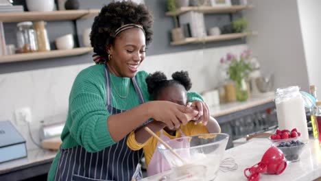 Happy-african-american-mother-and-daughter-adding-egg-to-bowl-in-kitchen,-slow-motion