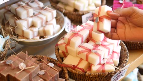 a woman's hand is shown picking up a bar of soap from a basket of wrapped soap bars.