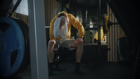 exhausted man in gym wipes face with towel between workout sets
