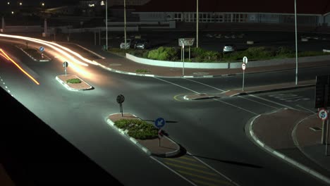 un rápido ritmo nocturno de larga exposición del lapso de tiempo de los coches que pasan por una intersección ocupada dejando largos rastros de luz detrás de ellos