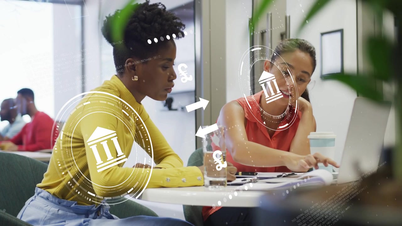 Two women leaning table and pointing causing financial icons circling laptop while planning budget