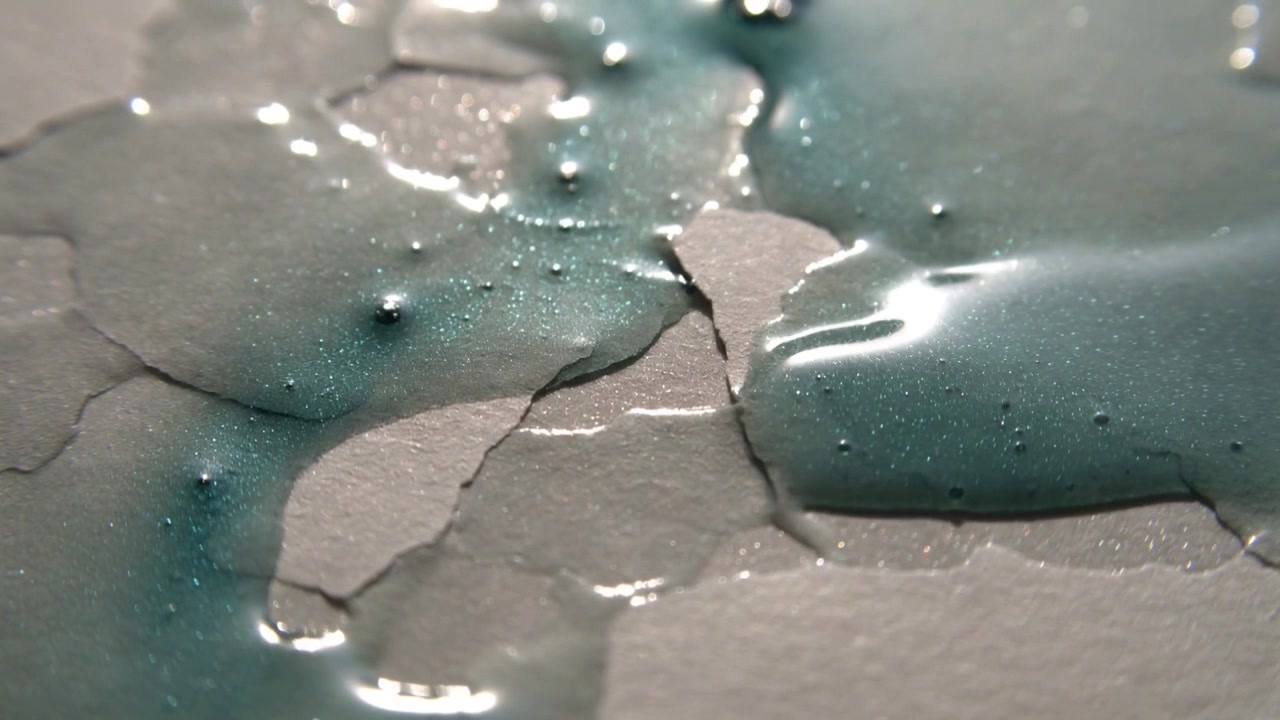 Spreading teal liquid puddle, droplets contacting textured paper causing merging and fiber wetting