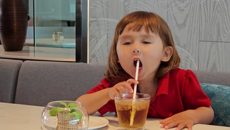 little girl drinking juice through a straw at home