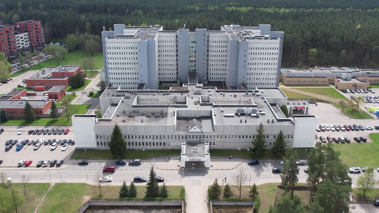 Drone ascends and pulls back from the hospital complex with forest behind