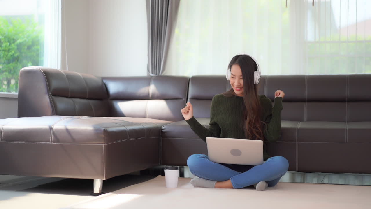 Quarantine can be fun, a young Asian woman sitting on the floor with a laptop playing music through headphones and dancing