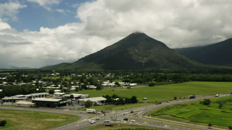 Descending-Aerial-Backwards-shot-of-driving-cars-on-asphalt-road-in-scenic-landscape-of-Australia-with-massive-overgrown-mountains-during-cloudy-day