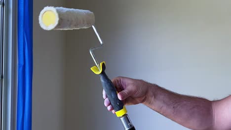 Día-De-Pintura,-Pintor-Masculino-Colocando-Un-Rodillo-De-Pintura-En-Un-Poste-En-Una-Habitación-Con-Paredes-Blancas