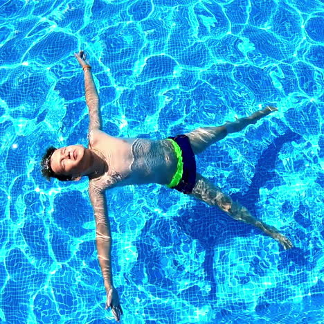 young boy in the swimming pool. teenager lying on his back on the water surface in a sunny day. blue clear water of a pool and a boy swimming.