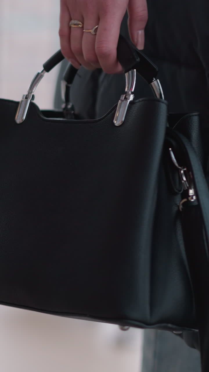 vista de ángulo bajo de una mujer en vaqueros llevando un bolso negro, de pie cerca de una barandilla de hierro con el paisaje urbano visible a través de una ventana de vidrio, reflejando el estilo de vida urbano moderno