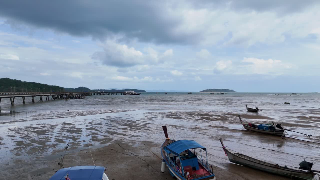 Aerial view of boats stranded at low tide near a pier in Phuket, Thailand, under cloudy skies, capturing serene coastal life