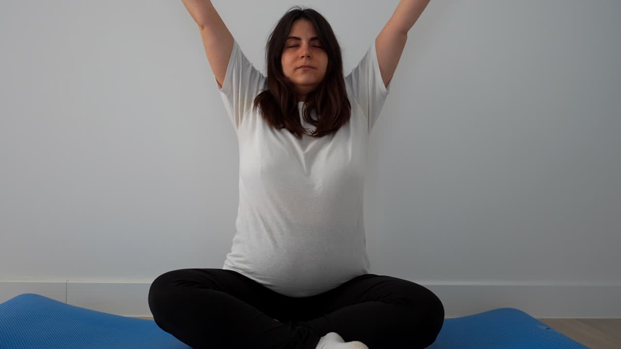 Pregnant woman doing seated breathing exercises at home with eyes closed for calm focus