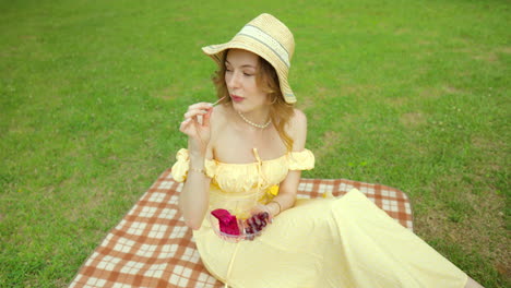 mujer joven en vestido amarillo disfrutando de un picnic en el parque comiendo fruta y leyendo