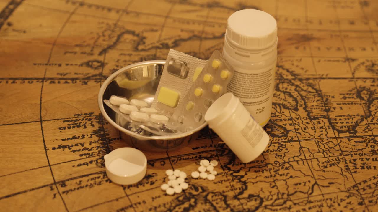 A cinematic slow zoom shot showing various medicine bottles, blister packs, and tablets arranged on a vintage wooden table