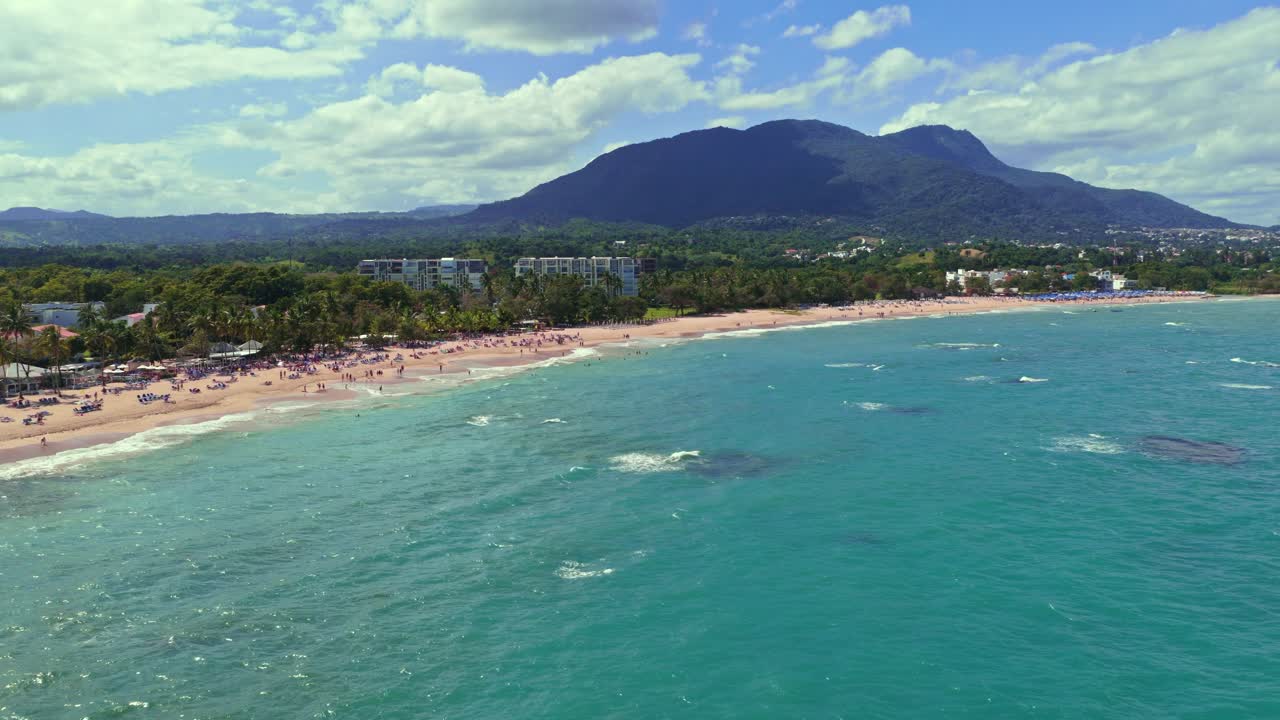 Ampia vista con drone dell'oceano e della spiaggia di Playa Dorada con catena montuosa sullo sfondo, Puerto Plata, Repubblica Dominicana. Avanzamento aereo, spazio per il testo