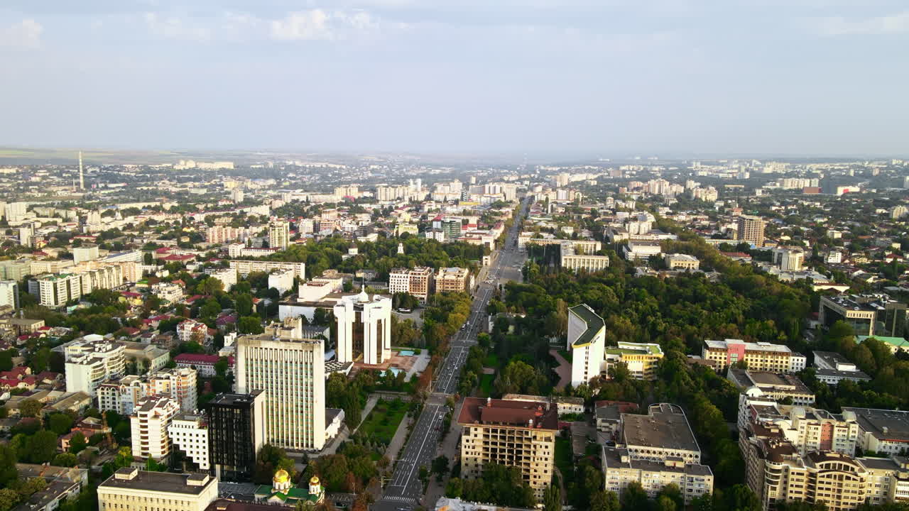 Aerial drone view of Chisinau downtown. Panorama view of multiple buildings, roads with moving cars and lush trees. Sunset. Moldova