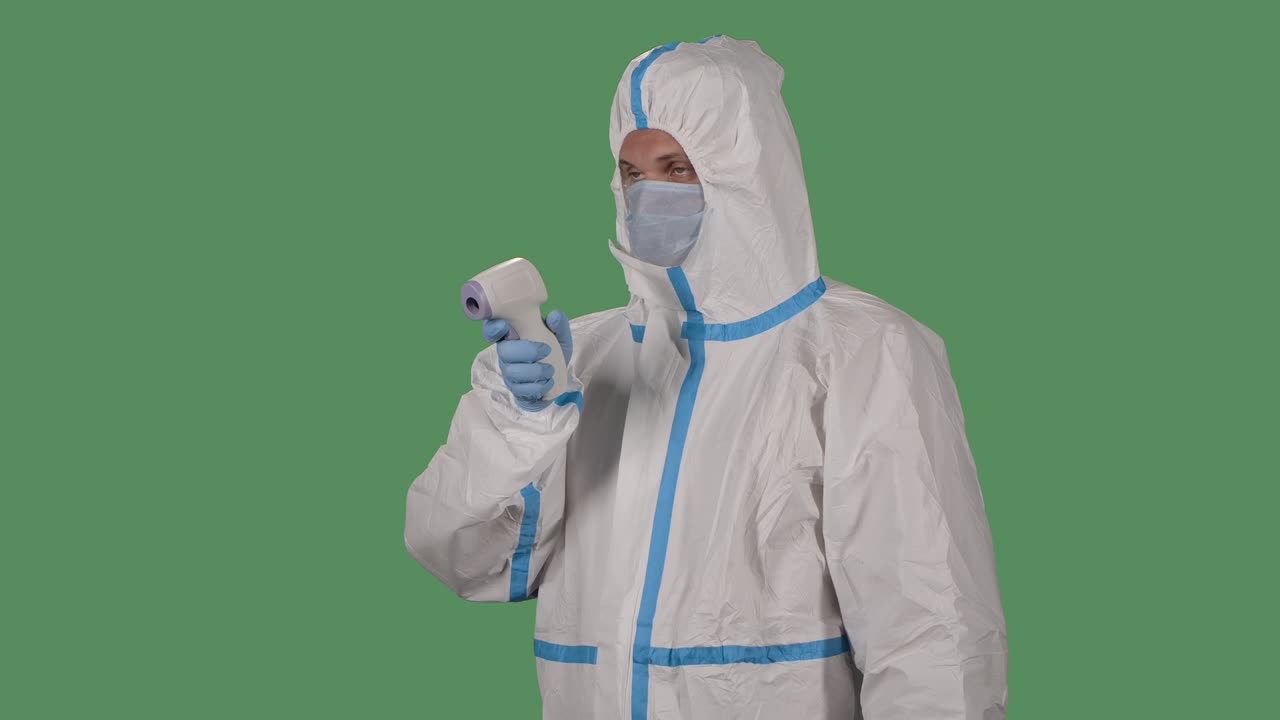 retrato de un hombre con un traje de protección y una máscara médica mide la temperatura con un termómetro sin contacto. pantalla verde, tecla de croma. cámara lenta. primer plano