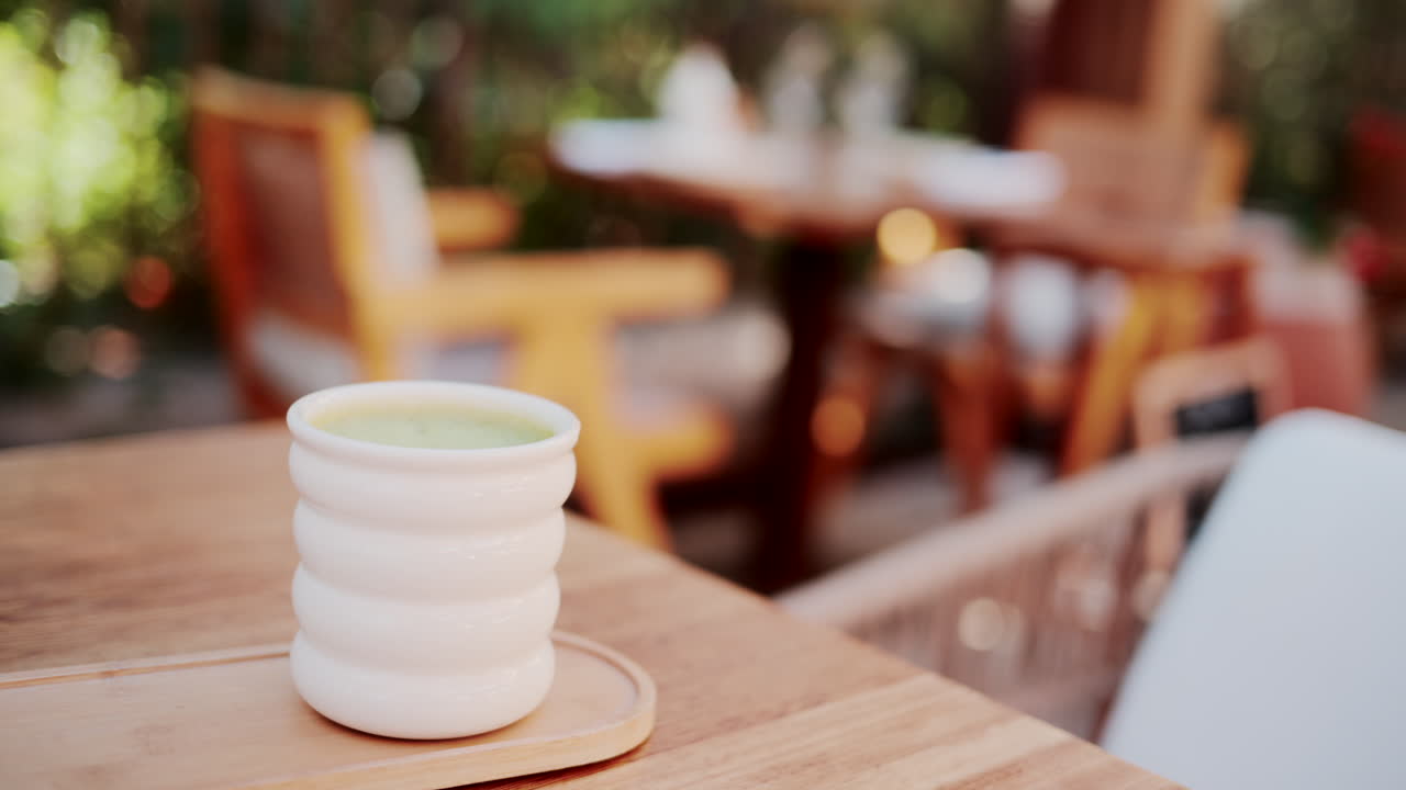 White ceramic cup of green matcha latte on a wooden table in a bright outdoor cafe