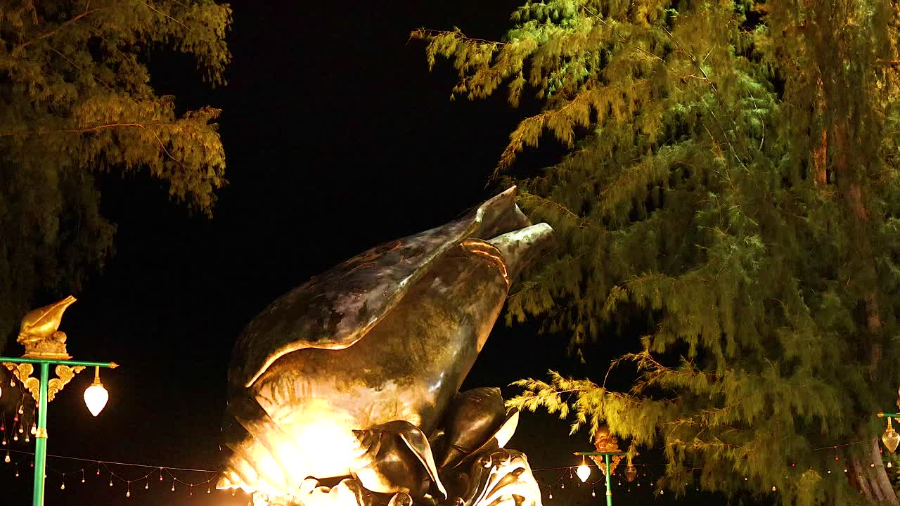 A large shell statue is beautifully lit at night, surrounded by trees and streetlights, creating a serene atmosphere