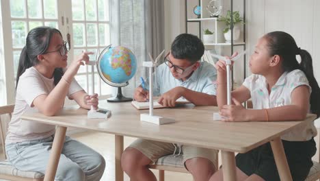 asian group of thoughtful kids study about ecology problems and their solution with wind turbine model and globe at school. renewable energy