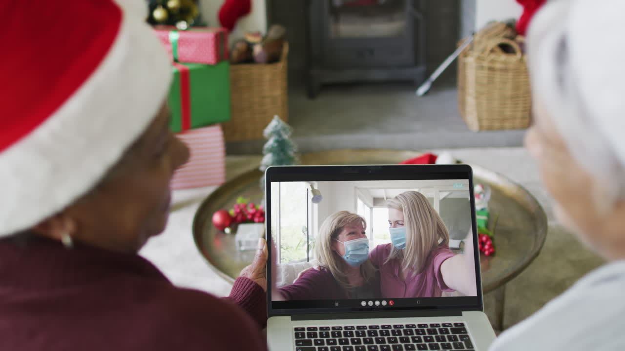 diversas amigas mayores que usan una computadora portátil para una videollamada de navidad con la familia en la pantalla
