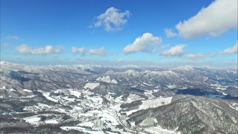 a drone aerial view of a frozen mountain range with snow and clouds on a bright blue sky day